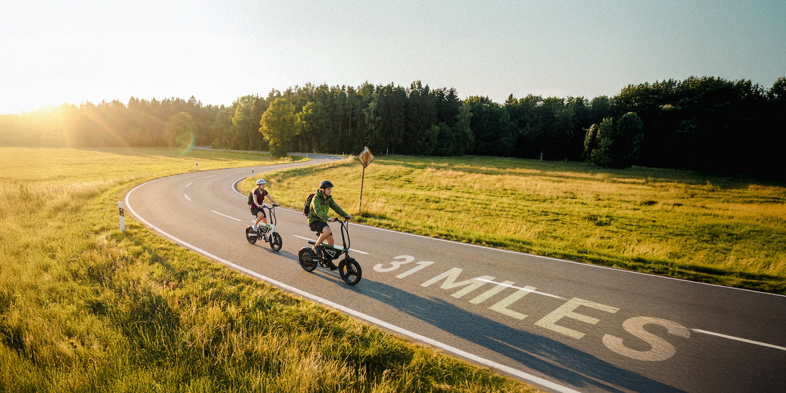 An aerial view captures two riders traveling along a winding countryside road with 