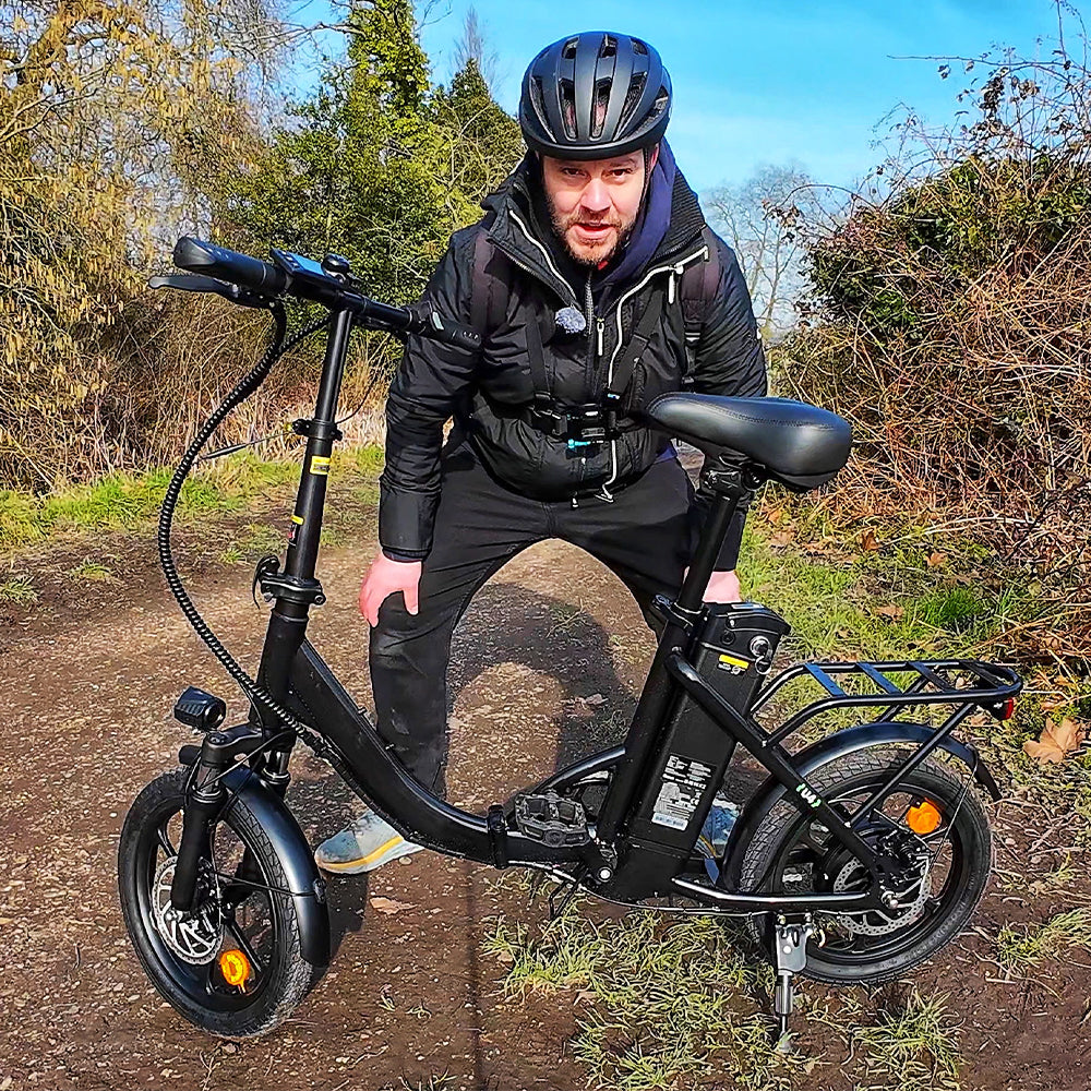 An outdoor review scene features the iScooter U4 electric bike parked on a woodland trail beside a helmeted rider. The image highlights the low step-through frame, removable battery, rear cargo rack, front suspension, and compact wheel design, showcasing the iScooter U4 as a practical and comfortable option for everyday commuting and recreational rides.
