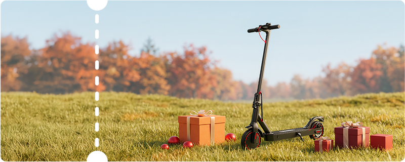 Scenic outdoor product showcase featuring a sleek black iScooter i9 electric scooter placed on a grassy field against blurred autumn trees and holiday gift boxes. Built for daily urban transport, this lightweight e-scooter includes puncture-proof honeycomb tires, a folding aluminum frame, red accent cabling, and a rear disc brake for efficient, hassle-free travel.