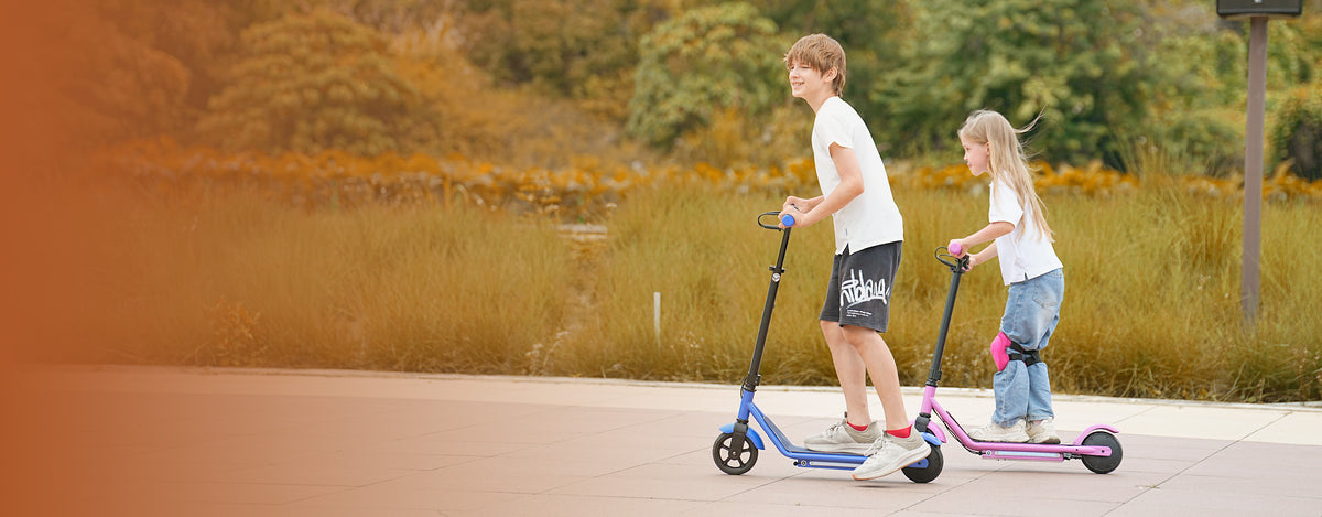 Two happy children riding colorful iScooter IK3Pro kids electric scooters along a smooth outdoor park pathway. Engineered specifically for young riders, this lightweight e-scooter features height-adjustable handlebars, vibrant ambient frame lighting, smooth magnetic charging, and dual brake safety systems to deliver a secure, exciting, and growing outdoor riding experience.