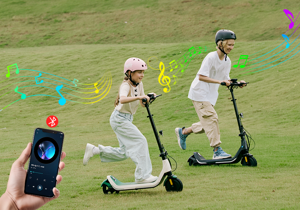 Hand holding a smartphone connecting to the iScooter iK5 electric scooter via Bluetooth music playback, allowing kids to stream music through built-in speakers while riding outdoors on grassy park paths.