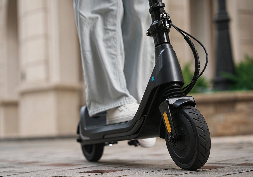 Detailed extreme close-up of the front treaded tire on the iScooter iK5 electric scooter, displaying its shock-absorbing rubber design, front fork suspension, side reflector, and sturdy wheel assembly engineered for optimal grip on paved surfaces.