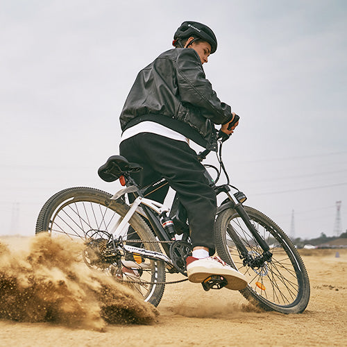 Rider maneuvering dynamic iHoverboard M50 electric mountain bike with integrated battery pack, responsive suspension, and disc brakes, kicking up sand on rugged terrain. The M50 delivers long‑range endurance, smooth off‑road handling, and powerful acceleration — perfect for adventurous outdoor cycling.