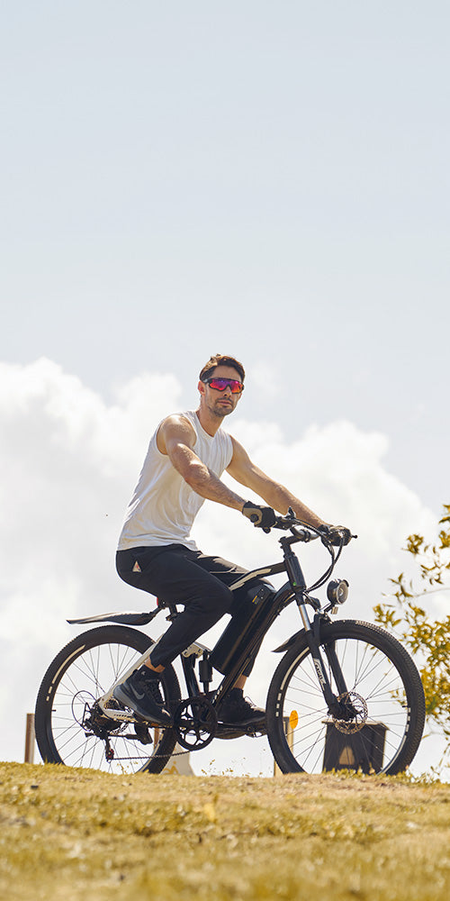 Rider cruising on sleek iHoverboard M50 electric mountain bike with integrated battery pack, thick tires, and front suspension, captured on grassy terrain under partly cloudy sky. The M50 provides extended riding range, smooth off‑road performance, and powerful acceleration — making it ideal for both outdoor adventures and everyday commuting.