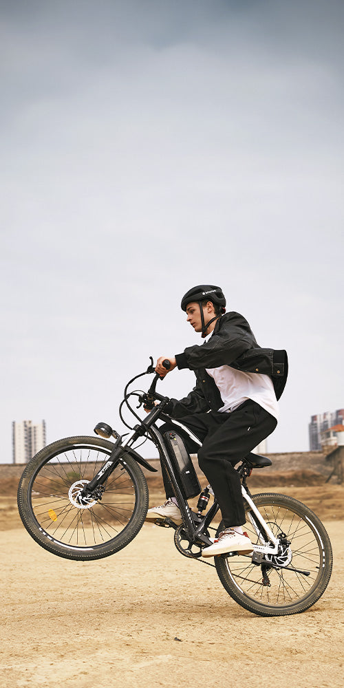 Rider performing a wheelie on rugged iHoverboard M50 electric mountain bike with integrated battery pack, responsive suspension, and disc brakes, showcasing balance and control on dirt terrain. The M50 offers extended riding range, powerful acceleration, and smooth off‑road handling — perfect for adventurous cycling and urban exploration alike.