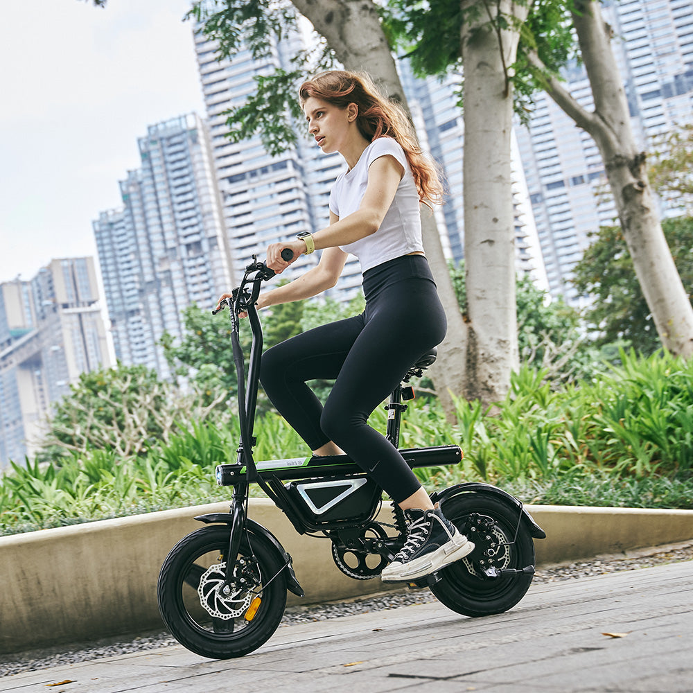 A rider navigates a landscaped urban park on the iScooter EB1S electric bike, with a modern city skyline in the background. The image highlights the compact folding frame, integrated battery, rear suspension, and comfortable upright riding position, showing how the iScooter EB1S combines smooth performance, portability, and everyday convenience for city commuting and leisure rides.
