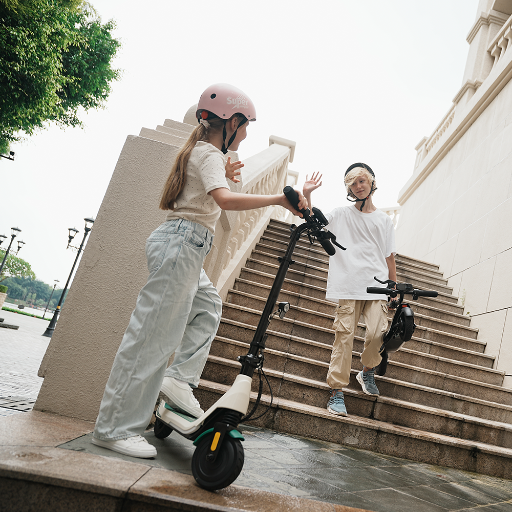 Young riders exchanging a high five beside outdoor stone stairs, featuring the iScooter iK5 electric scooter with its lightweight foldable frame, ergonomic handlebars, and safety reflectors that make transportation easy and fun for kids.