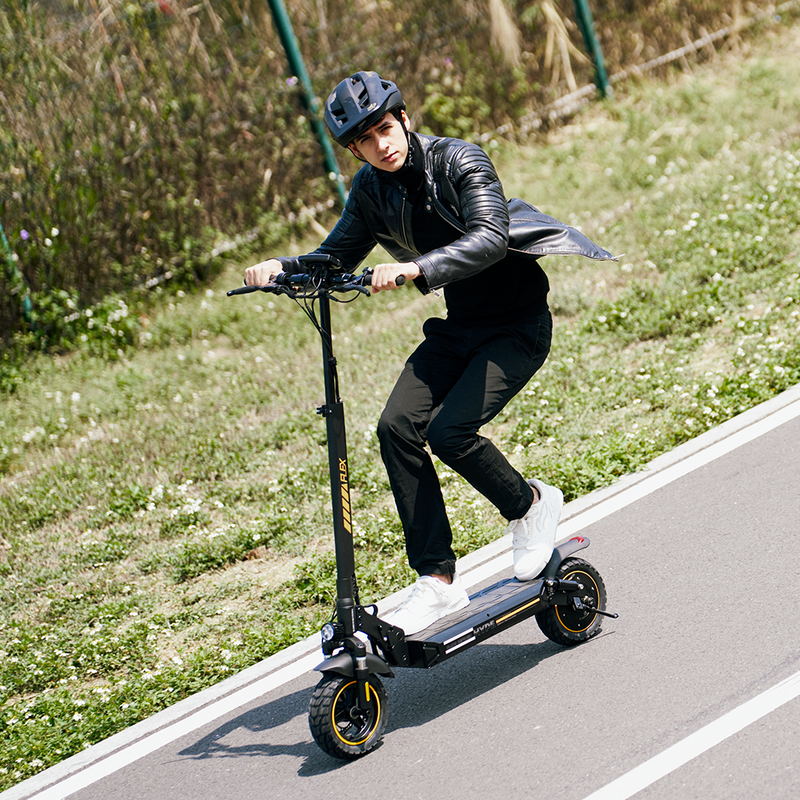 High‑performance black electric scooter with sturdy frame and thick tires accented in yellow, shown in motion on a paved path with greenery and fencing in the background, emphasizing durability, modern design, and smooth commuting performance.